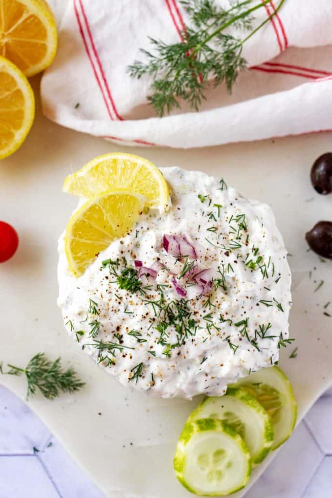 Overhead photo of Keto Tzatziki Sauce garnished with dill, lemon, and red onion.