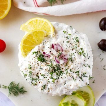 Overhead square photo of Keto Tzatziki Sauce garnished with dill, lemon, and red onion.