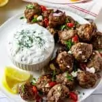 Square photo of lamb meatballs on a plate with a small bowl of dill garnished tzatziki sauce.