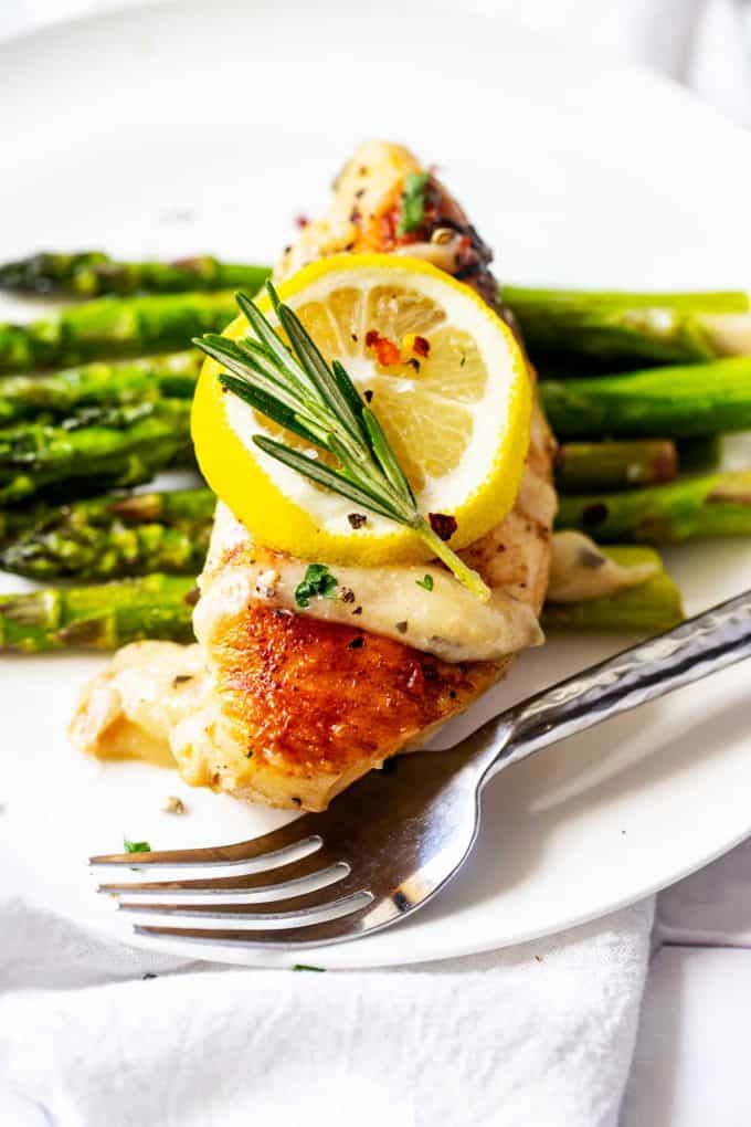 Close up photo of a white plate with Instant Pot Rosemary Chicken sitting on top of asparagus garnished with lemon and rosemary.