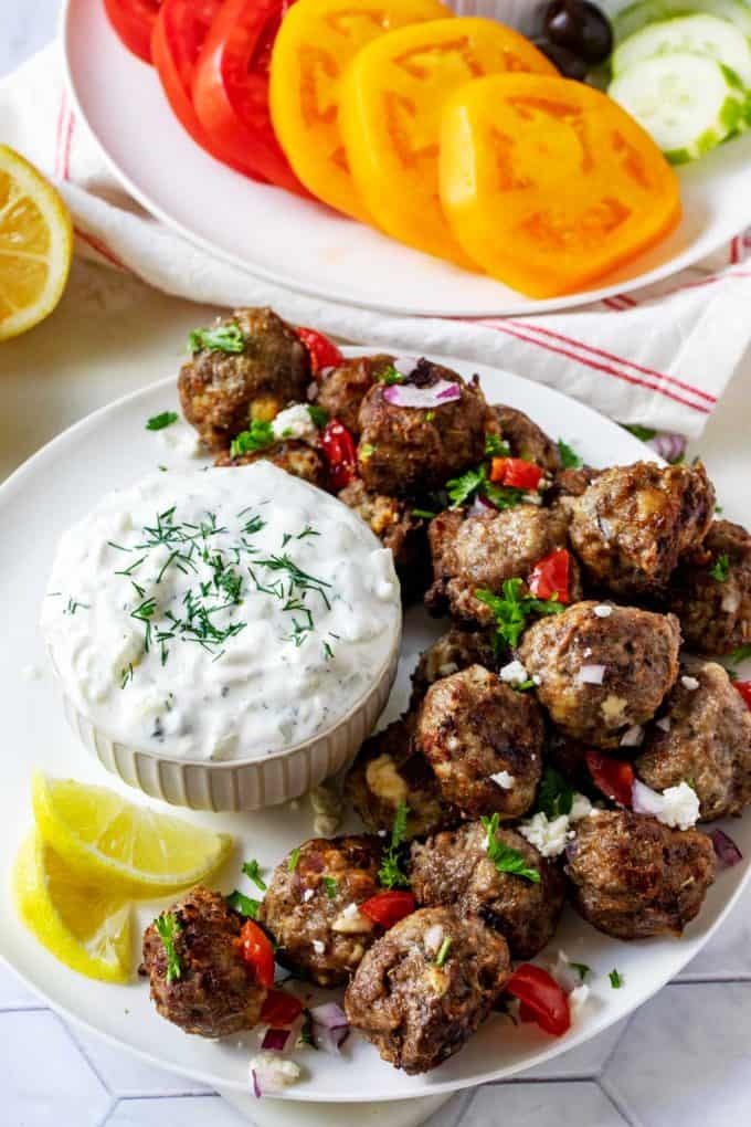 Photo of Keto Lamb Meatballs on a white plate garnished with parsley, feta, red onion, and tomato.