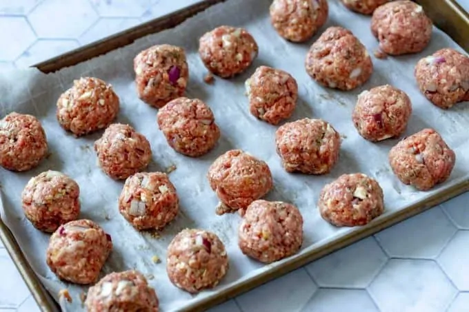 Photo of a parchment lined baking sheet with meatballs on it.