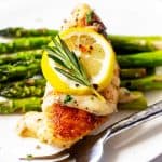 Square close up photo of a white plate with Instant Pot Rosemary Chicken sitting on top of asparagus garnished with lemon and rosemary.