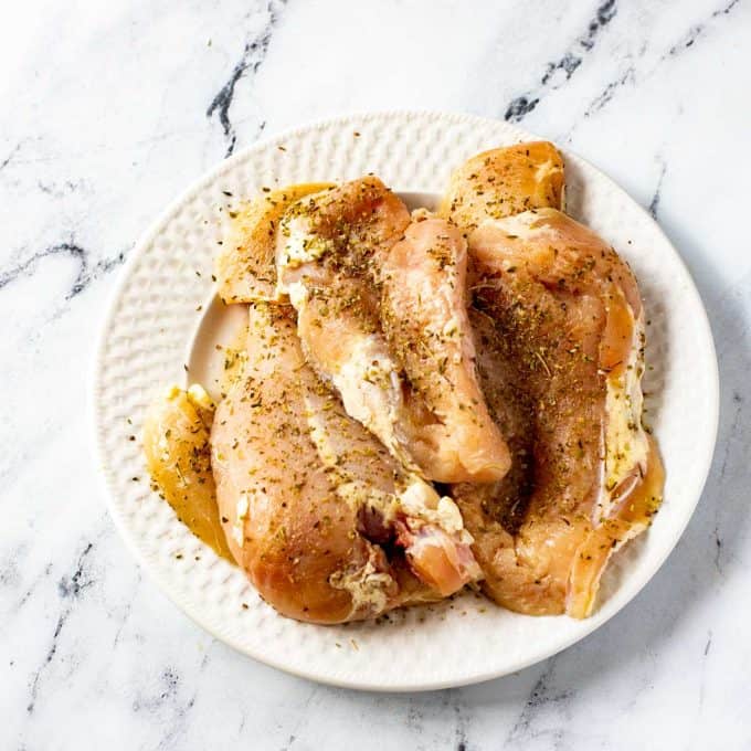 Seasoned Italian Chicken on a white plate ready to cook.