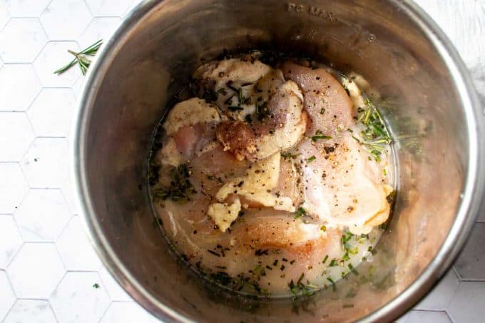 Photo of an Instant Pot with lemon juice, broth, rosemary, and seasoned chicken.
