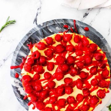 Overhead photo of a keto cheesecake topped with raspberries on a two tone marble stand.
