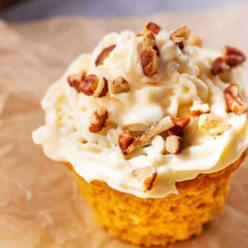 Close up photo of a Keto Pumpkin Muffin iced with cream cheese frosting and sprinkled with pecans.