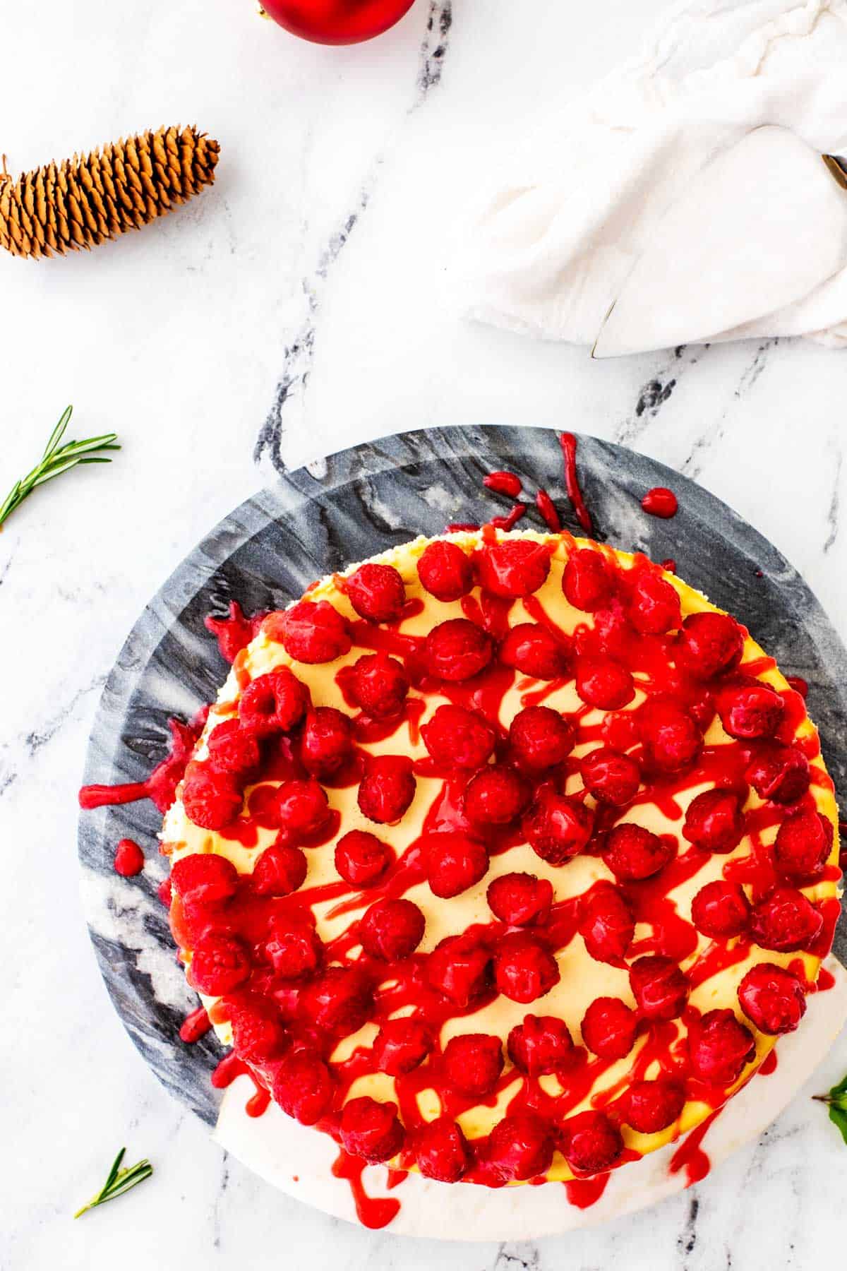 Overhead photo of a keto cheesecake topped with raspberries on a two tone marble stand.