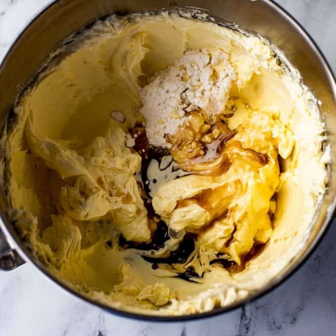 The bowl of a stand mixer with creamed cream cheese and maple syrup substitute, sweetener, and cream that have been added on top of it.