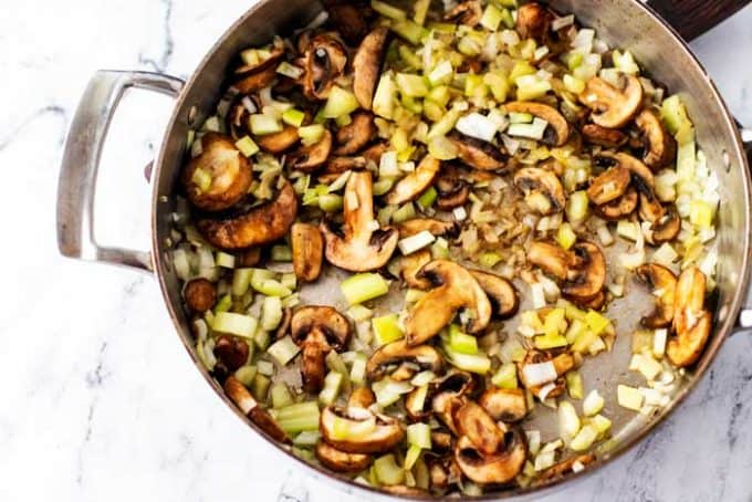 Celery, mushrooms, and onion being that have been cooked in a skillet.