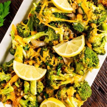 Square photo of a platter of cheesy roasted broccoli garnished with lemons.