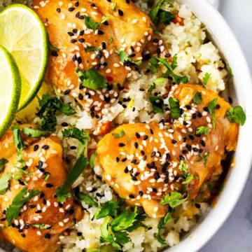 Square overhead photo of a white bowl of keto sesame chicken garnished with cilantro, lime, and sesame seeds.