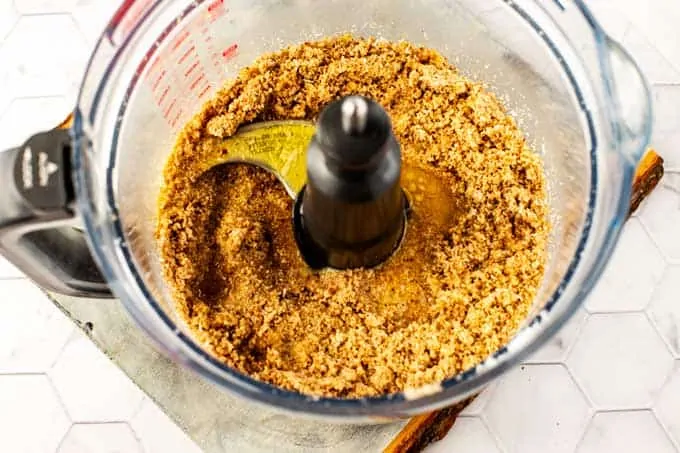 Photo of melted butter being added to pecans, coconut, Swerve, and salt in a food processor.