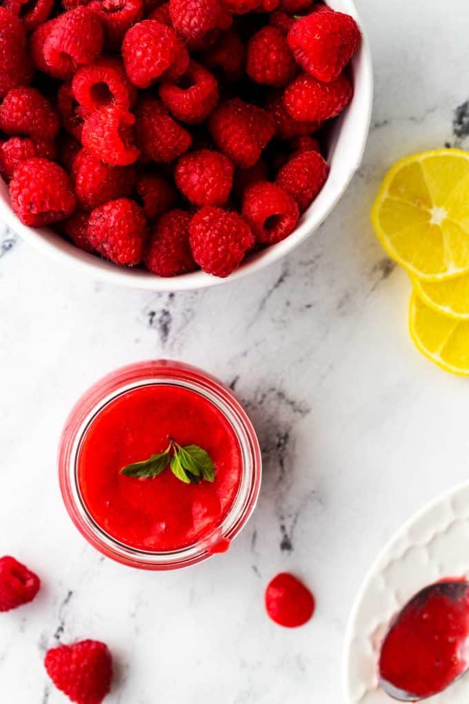 Photo of a small jar of keto raspberry sauce garnished with mint with a bowl of raspberry sauce.