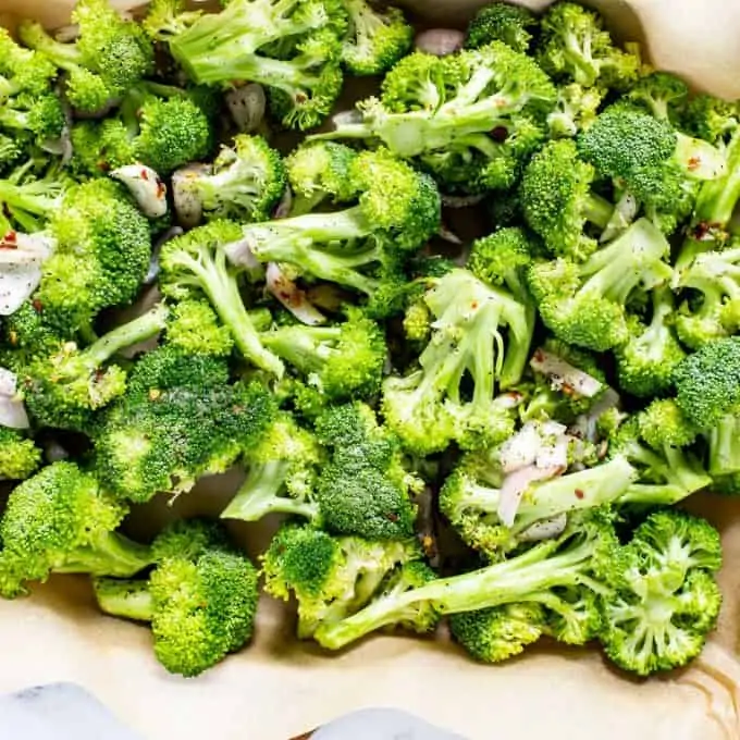 Raw broccoli and shallots on a parchment lined baking sheet.