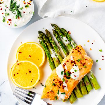 Square overhead photo of a white plate with Instant Pot Frozen Salmon on a bed of asparagus.