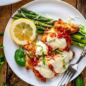 Square Overhead photo of keto chicken parmesan on a white plate against a dark wooden background.