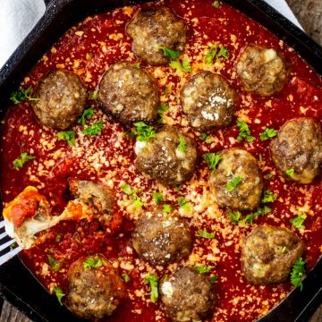 Square photo of a cast iron skillet with keto stuffed meatballs in marinara and a fork pulling a cheesy bite from it.