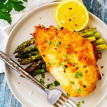 Square overhead photo of a plate of Keto Parmesan Crusted Chicken on a bed of asparagus.