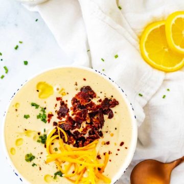 Overhead photo of a white bowl with Keto Cauliflower Soup garnished with bacon, chives, and shredded cheddar cheese.