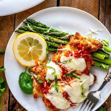Overhead photo of keto chicken parmesan on a white plate against a dark wooden background.