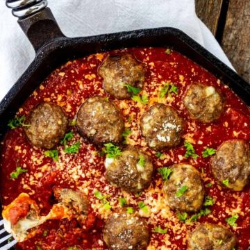 Photo of a cast iron skillet with keto stuffed meatballs in marinara and a fork pulling a cheesy bite from it.