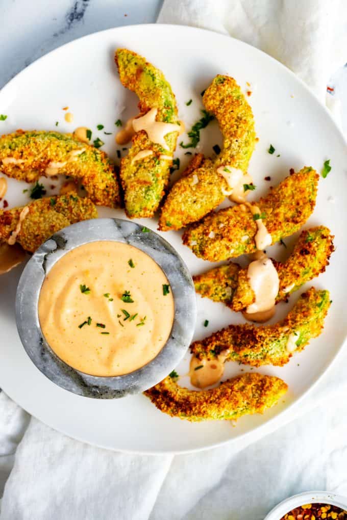Overhead photo of Keto Avocado Fries on a white plate with a small bowl of a spicy sauce.
