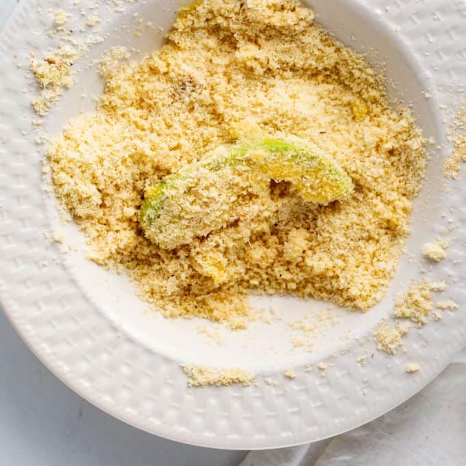 Photo of a piece of avocado being coated in a mixture of almond flour and parmesan cheese.