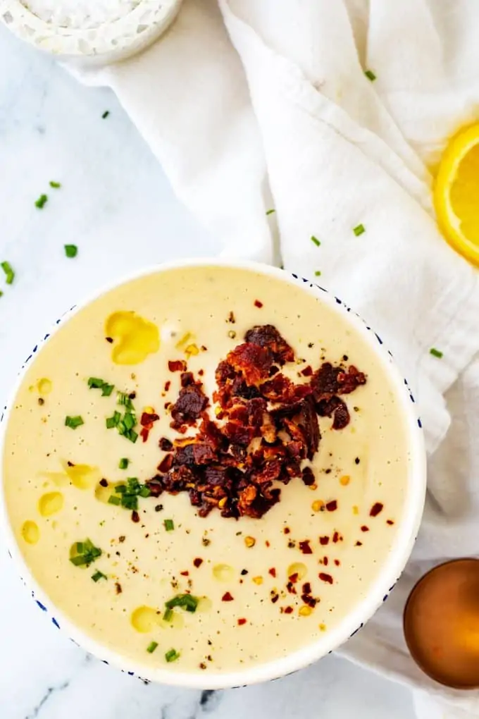 Overhead photo of a white bowl of keto Cauliflower Cheese Soup on a white background.