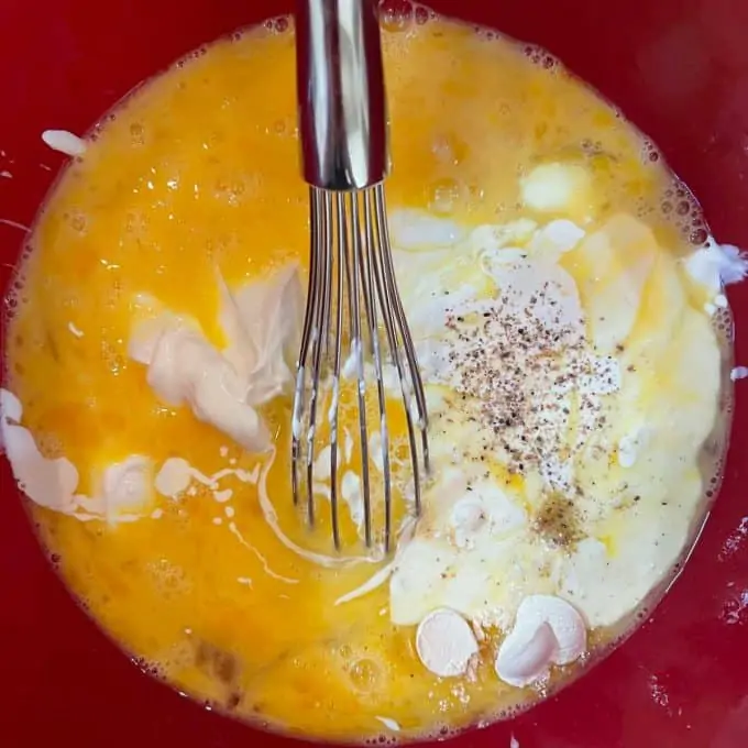 Photo of eggs in a red bowl beaten with sour cream, heavy cream, and seasonings.