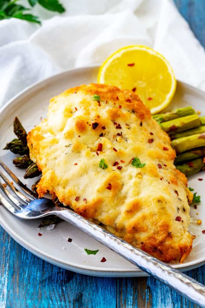 Side photo of a piece of keto parmesan crusted chicken on a plate with asparagus.