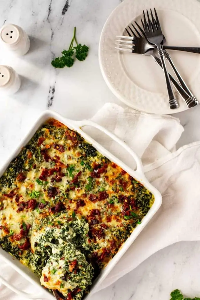 Overhead photo of a keto spinach casserole in a white casserole dish with a cheesy spoon pull.