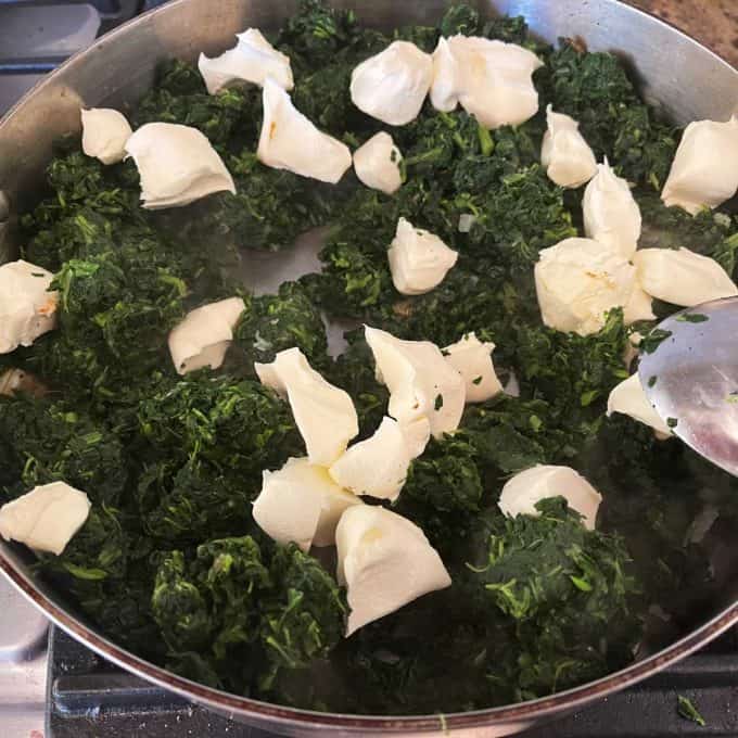Photo of spinach and cream cheese being added to sauteed onion and garlic in a skillet.