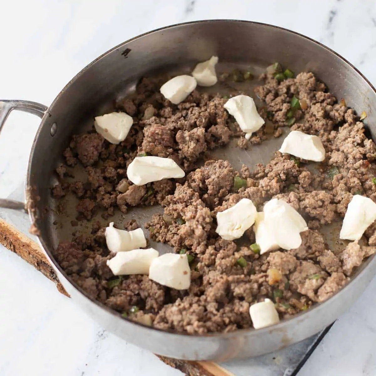 Photo of cream cheese being added to ground beef, onion and jalapeno in a skillet.