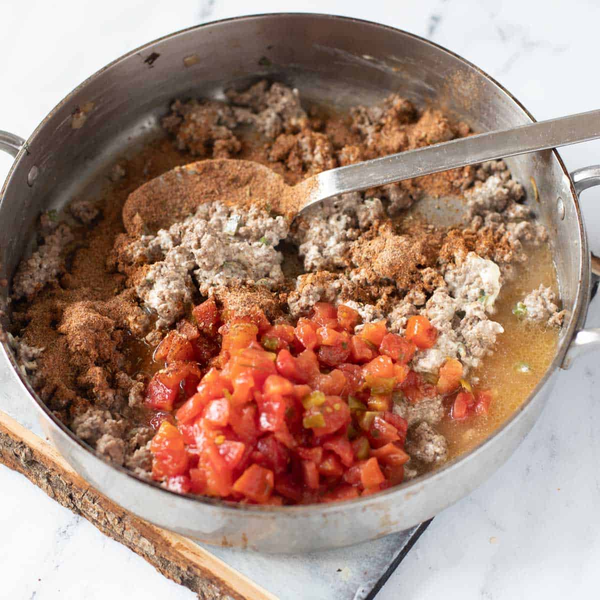 Photo of canned tomatoes and seasoning added to ground beef, onion, cream cheese and jalapeno in a skillet
