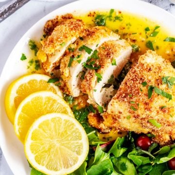 Square photo of buttery chicken kiev on a white plate garnished with parsley.