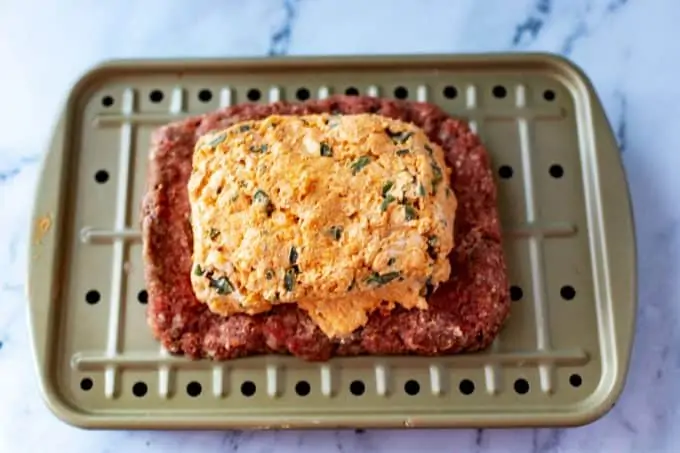 Photo of jalapeno popper mixture on top of the base of a meatloaf.