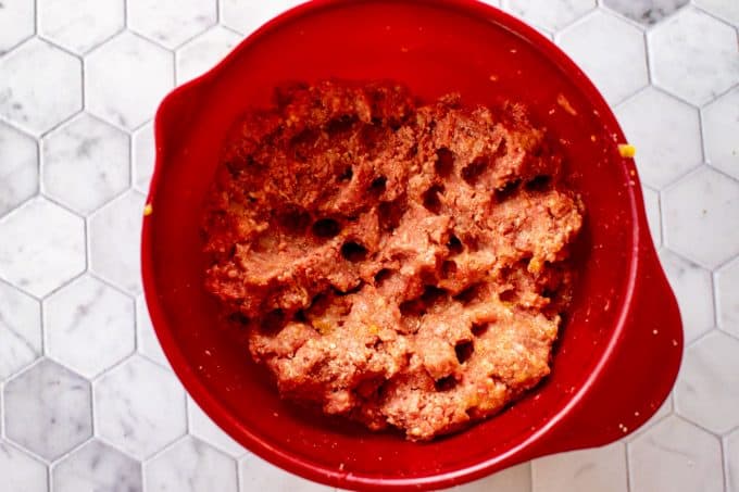 Photo of a red bowl with meat, parmesan, almond flour, seasonings, eggs, and gelatin that have been combined.