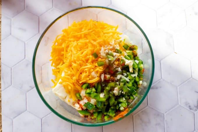 Photo of a glass bowl with cream cheese, cheddar cheese and chopped jalapeno.