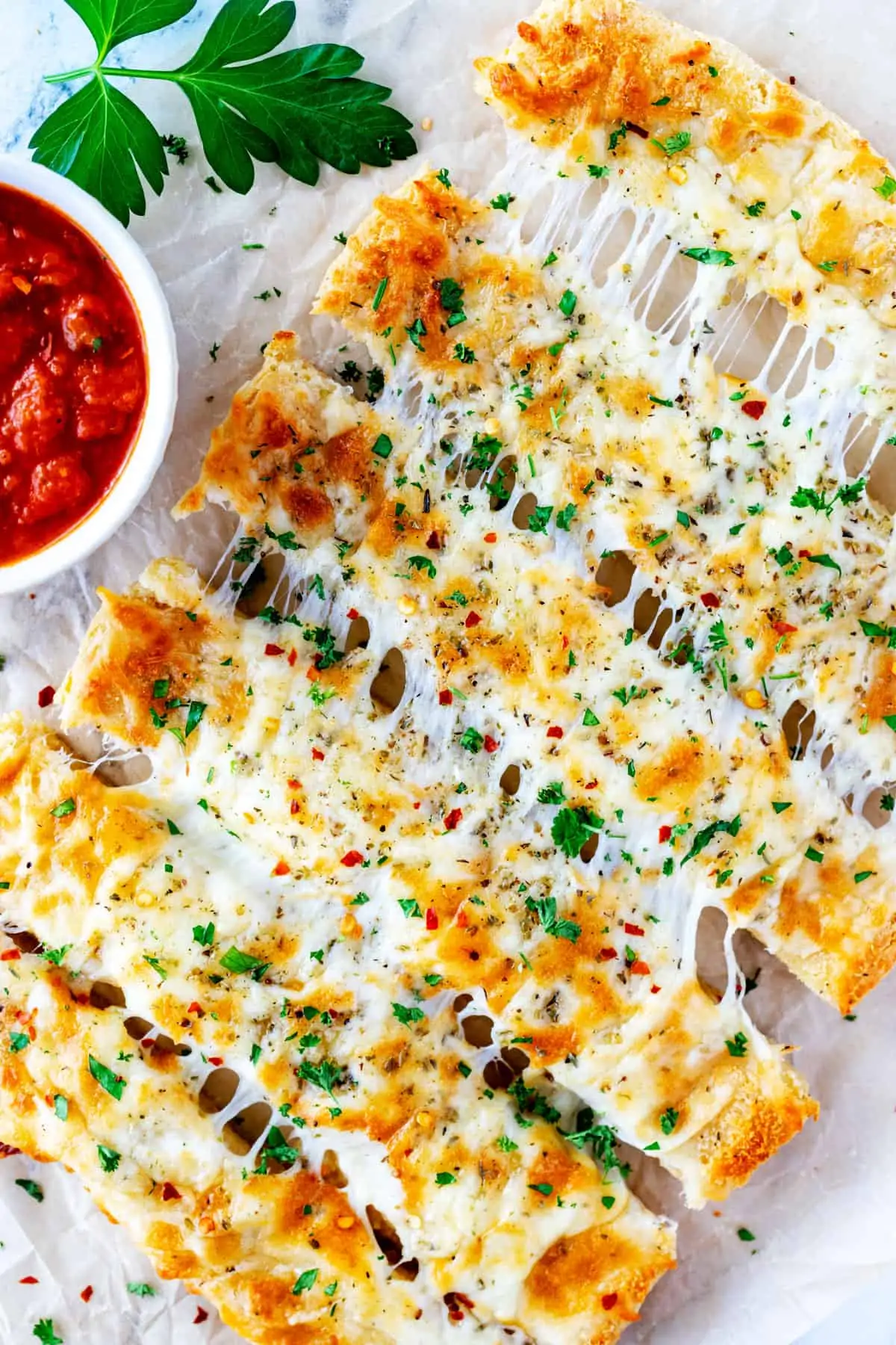 Overhead photo of keto cheesy breadsticks on parchment paper with a bowl of marinara by it.