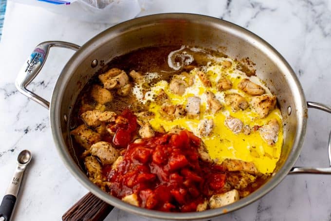 Photo of cooked chopped chicken in a skillet with canned tomatoes and heavy cream.