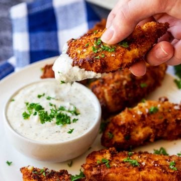 Square photo of a keto chicken tender being dipped into ranch dressing.