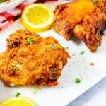Square photo of a white platter of Keto Fried Chicken garnished with parsley and lemons.