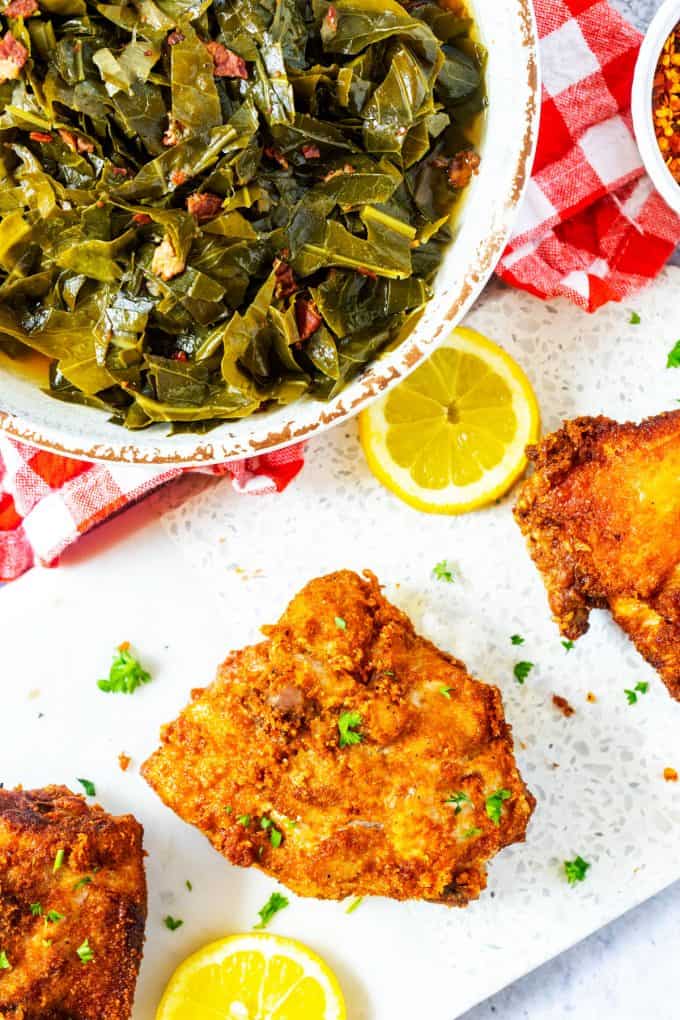 Photo of three pieces of Keto Fried Chicken on a white background with a bowl of collard greens next to it.