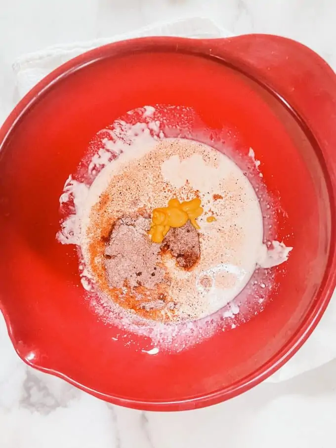 Photo of seasonings and mustard being added to a red bowl.
