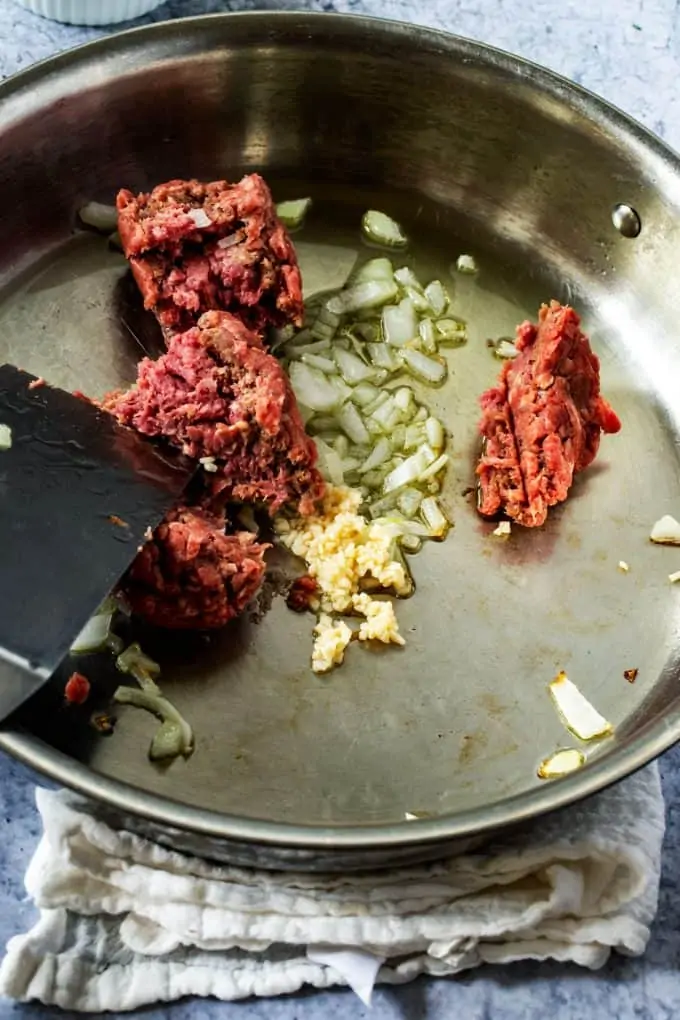 Photo of ground beef being added to a skillet with onion and garlic.