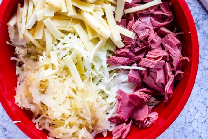 Photo of cabbage, chopped corned beef, sliced cheese and sauerkraut in a large bowl.