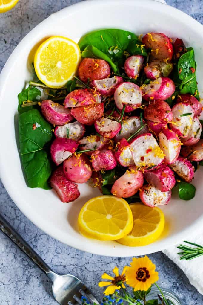 Close up photo of Keto Roasted Radishes on a bed of greens garnished with lemons and lemon zest.