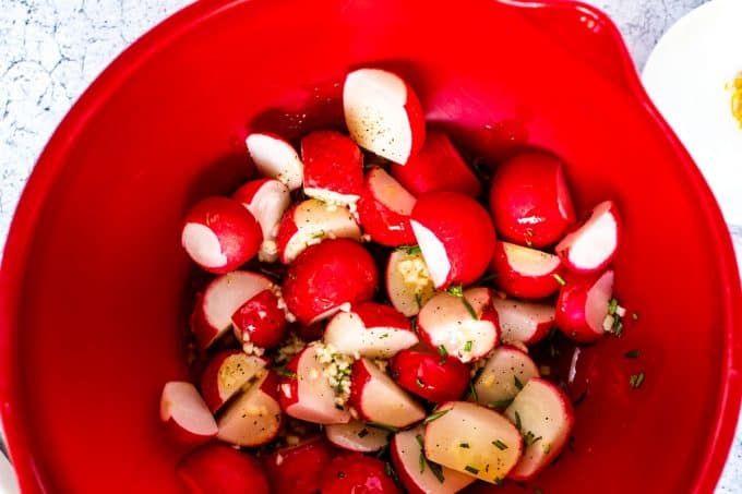 Photo of a red bowl with radishes being tossed with butter.