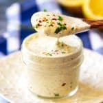 Square photo of a spoon of creamy Keto Ranch Dressing being lifted from a small jar.